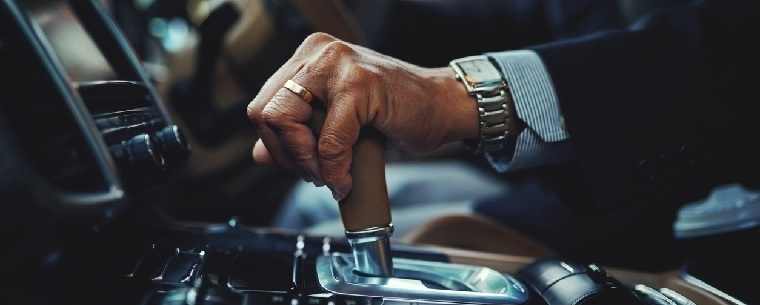 man wearing watch changing gear in car