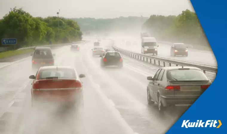 Cars are driving down the motorway in heavy rain. The roads are wet and their tyres kick up spray.