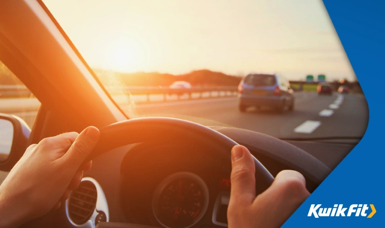 Hands on a steering wheel as a person drives on a motorway.