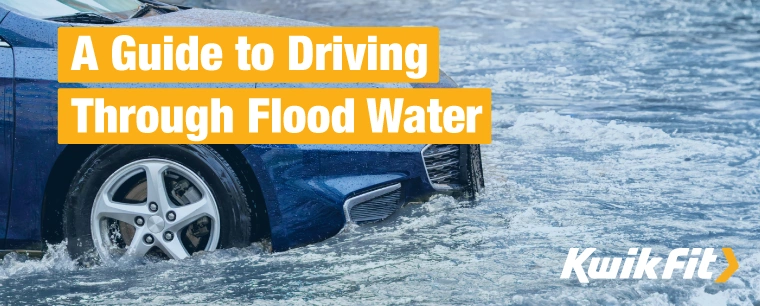 A blue car driving through flood water.