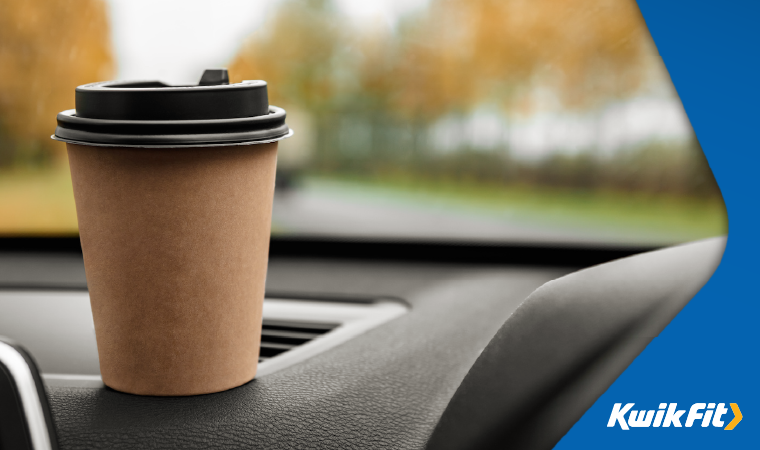 Takeaway coffee cup on top of a vehicle dashboard.