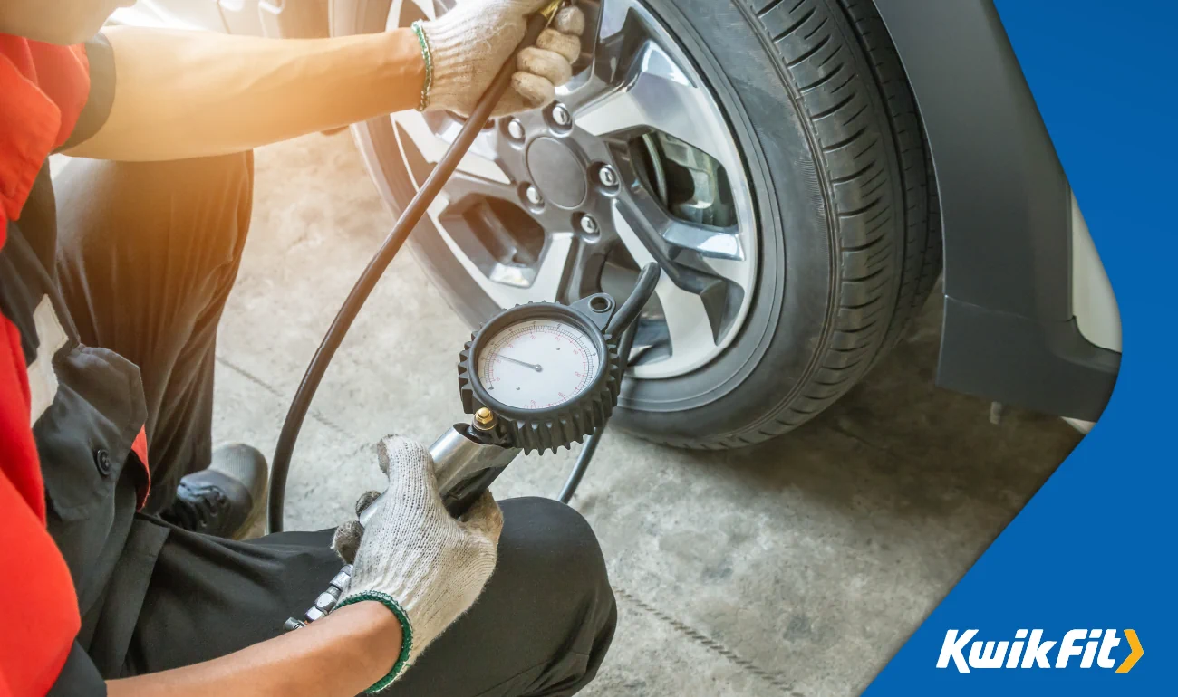 Technician using a tyre pressure gauge to pump a car tyre.