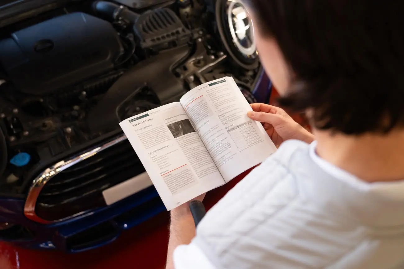 Person checking the wheel and pressure page of their manual whilst the bonnet of their car is up.