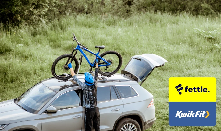 Person with blue bike helmet on putting their bike back on the roof-mounted bike rack on their car.