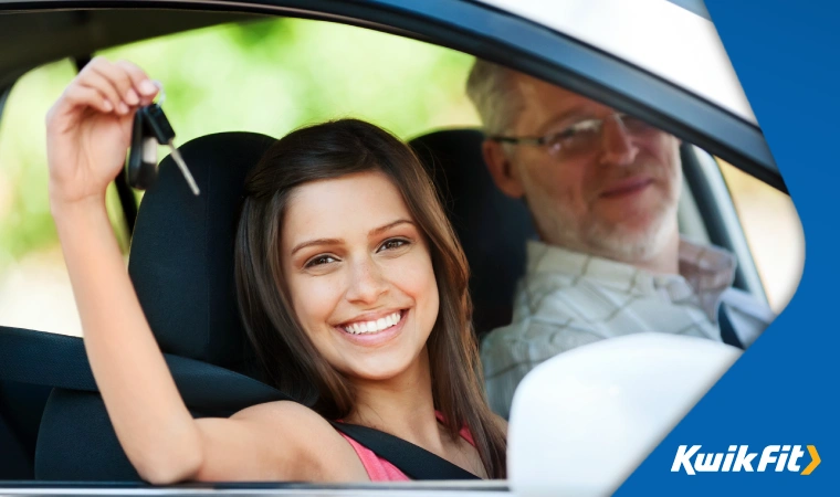 A newly-passed driver holding their car key triumphantly out of the car window.