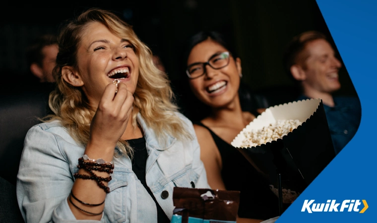 People laughing at a cinema whilst sharing popcorn.