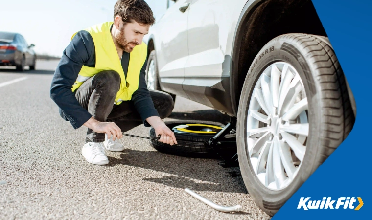 A person in a high vis changing a tyre at the side of the road.