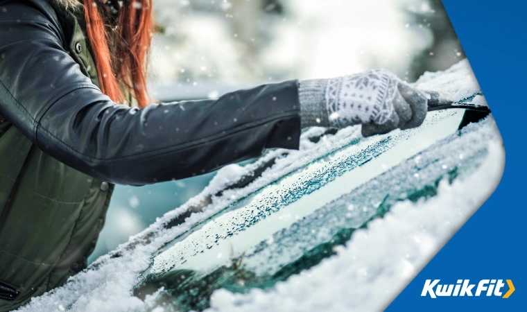 Person scraping ice off their car window while it snows.