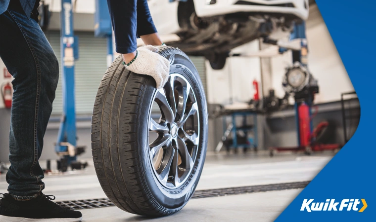 Auto technician wheeling replacement wheel fitted with run flat tyre.