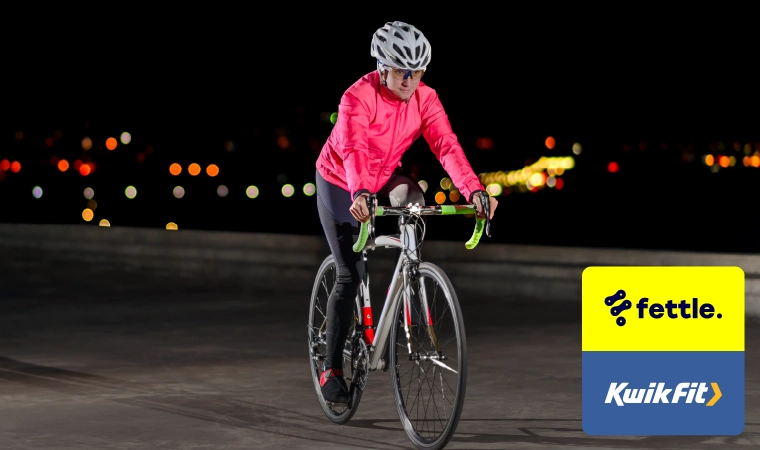 Person riding a bike in the dark with a pink jacket, black trousers and white helmet on.