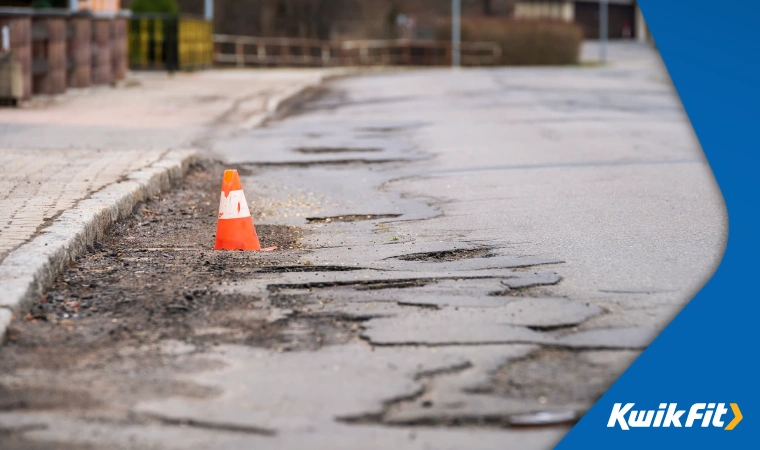 A solitary orange traffic cone is placed in an area of extensive road erosion.